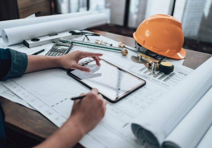 Engineering working with drawings inspection on tablet in the office and Calculator, triangle ruler, safety glasses, compass, vernier caliper on Blueprint. Engineer, Architect, Industry and factory concept.